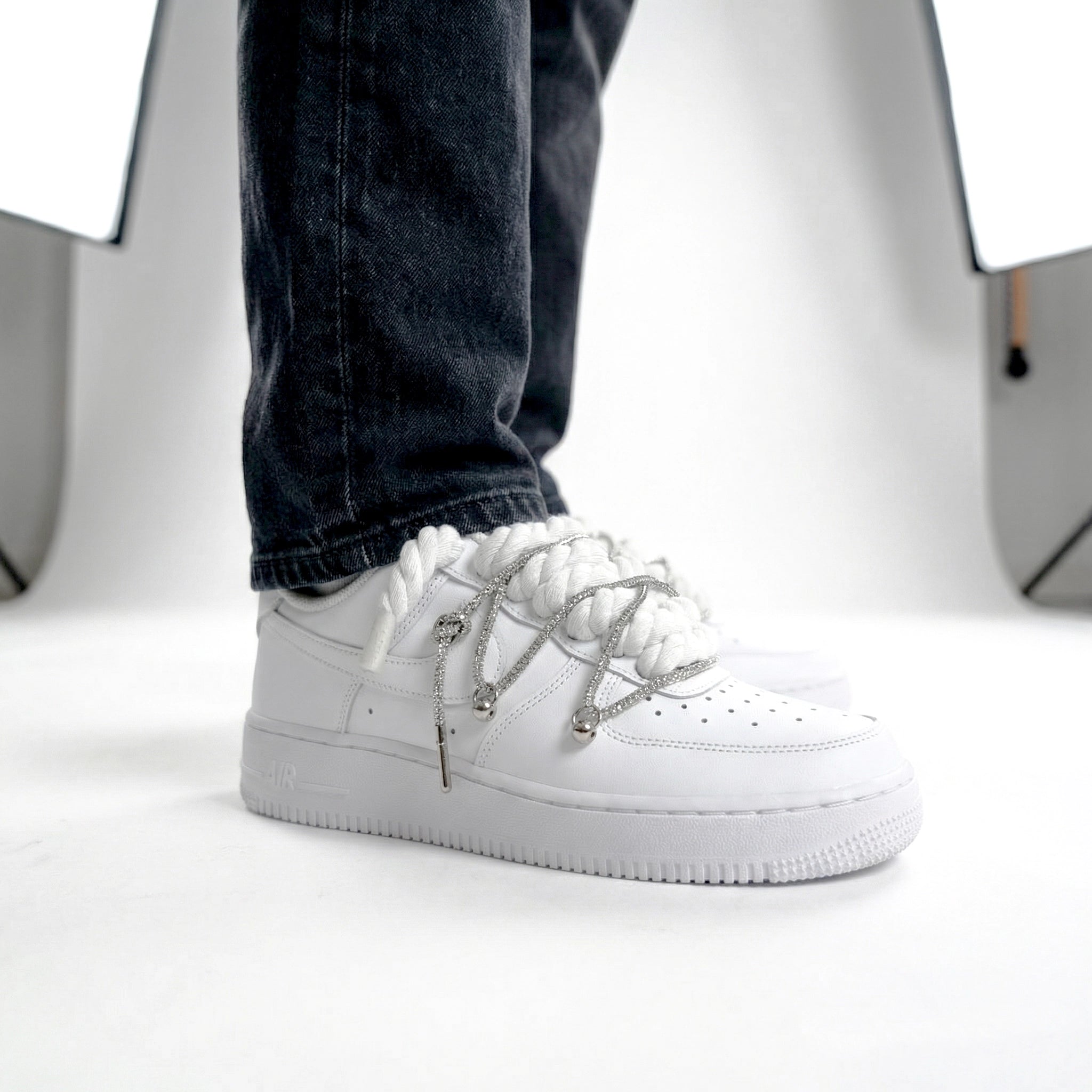 Detail bielych Nike Air Force 1 s bielymi rope laces a striebornými ozdobami na nohách
