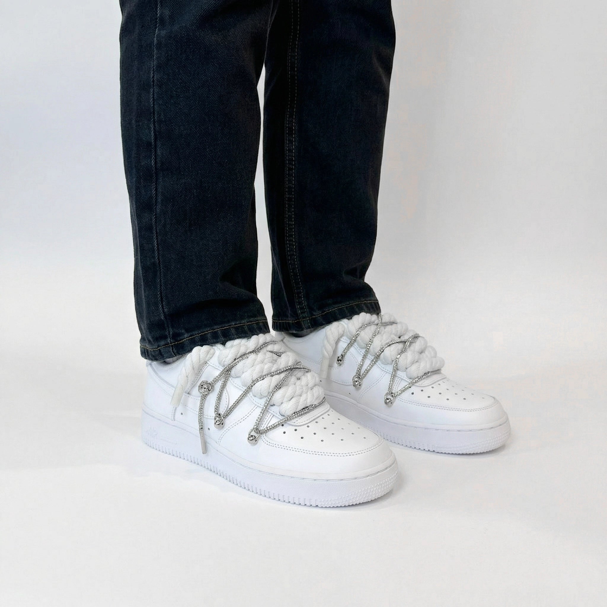 Predný pohľad na biele Nike Air Force 1 s bielymi rope laces a striebornými ozdobami na nohách