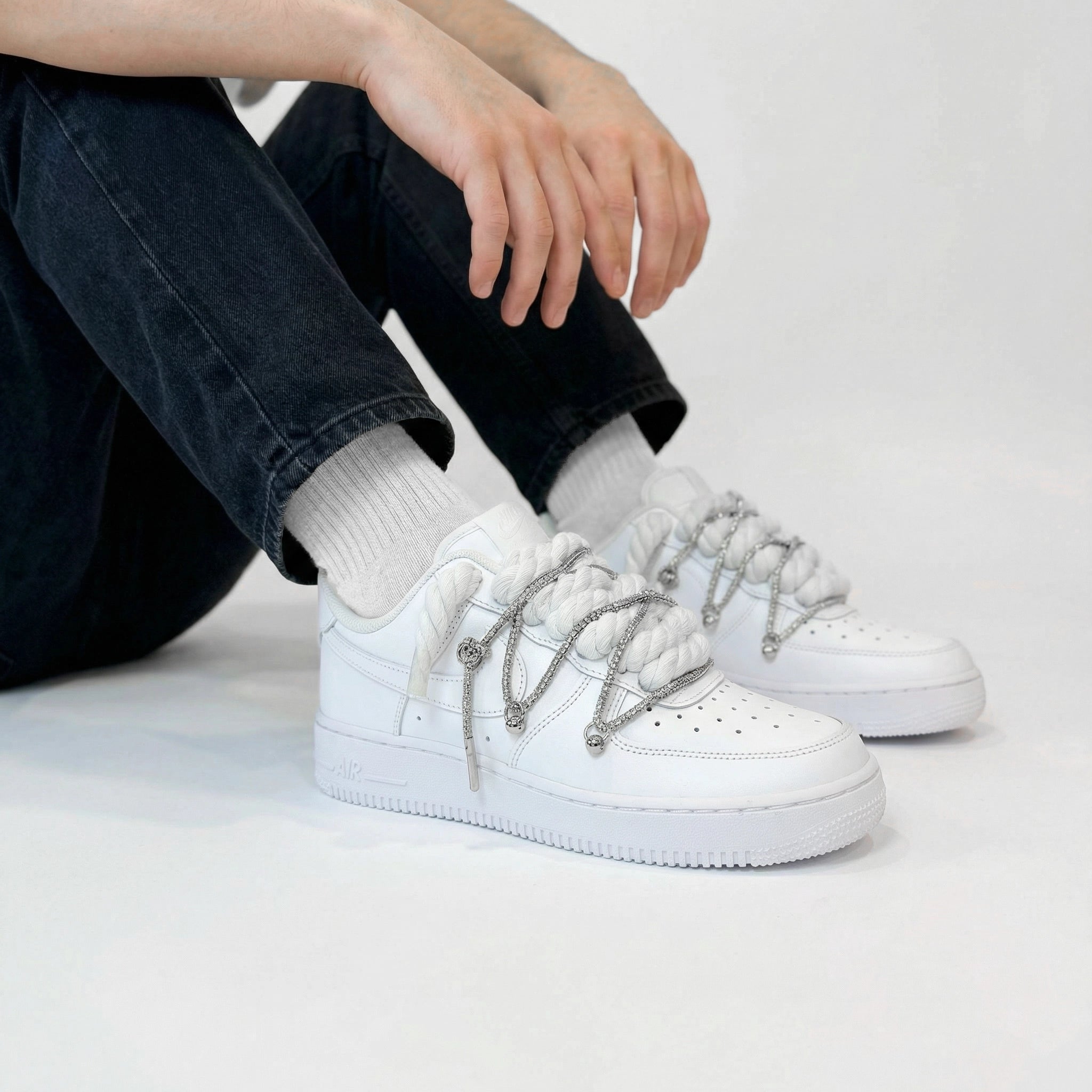 Biele Nike Air Force 1 s bielymi rope laces a striebornými ozdobami na nohách